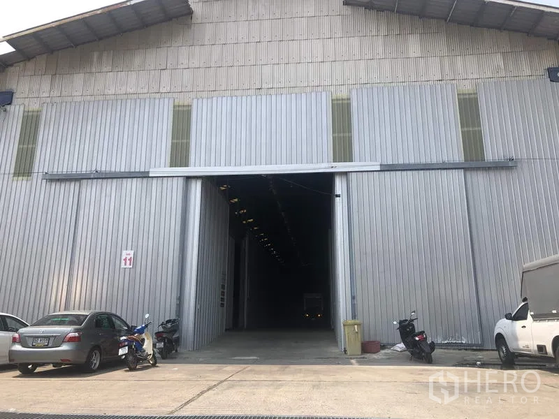 Warehouse for rent in Pak Kret, Nonthaburi - Large sliding-door entrance of a metal-clad warehouse with parking area at the front in Pak Kret, Nonthaburi.
