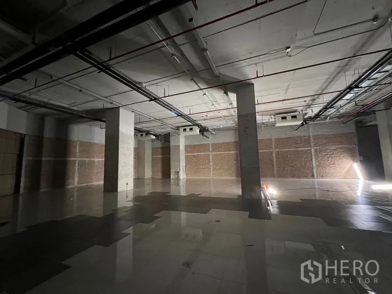 Retail Space for rent - Wide view of unfinished retail floor with multiple columns and overhead pipes and ducts.
