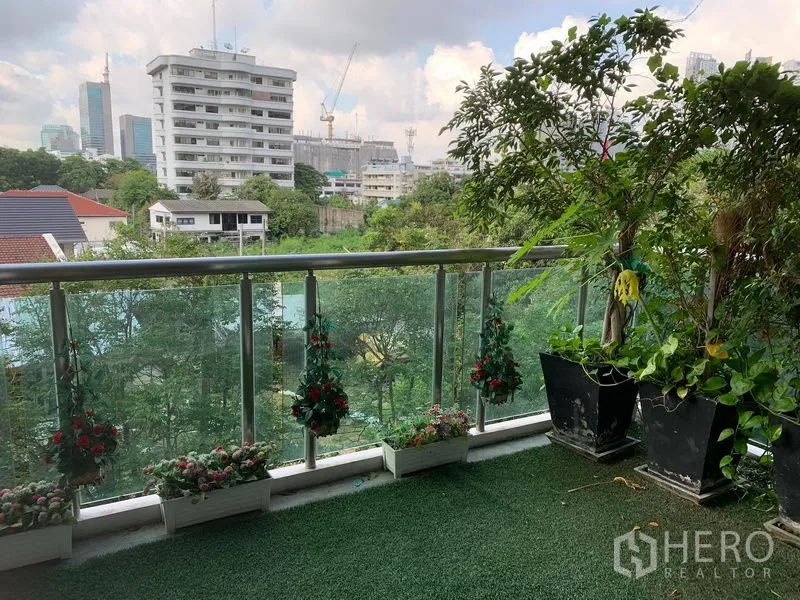 Condominium for sale in Khlong Toei, Bangkok - Leafy balcony with artificial grass, potted plants and treetop and city views.