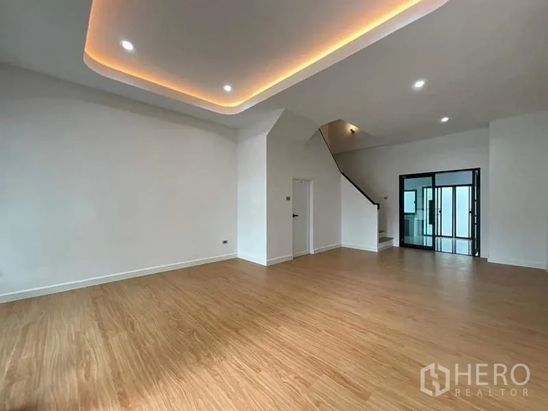 联排别墅 出售在Watthana, Bangkok - 大客厅，天花灯带、楼梯与推拉玻璃门