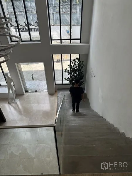 Home Office for rent in Phra Khanong, Bangkok - View down a staircase to a double-height entry with full-height windows.