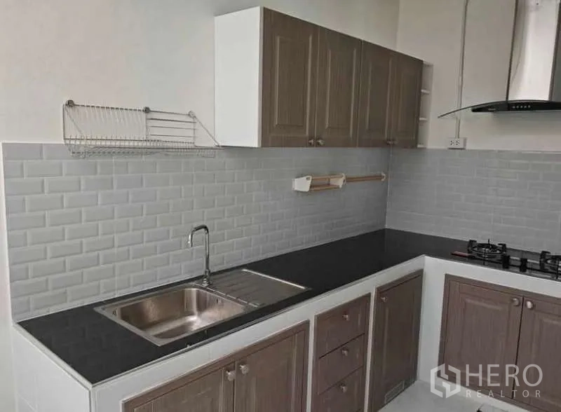 Townhouse for rent in Bang Phli, Samut Prakan - L-shaped kitchen with grey subway-tile backsplash, black countertop, hob, hood and sink.