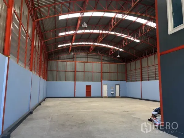 Warehouse for rent or sale in Sai Noi, Nonthaburi - High-ceiling warehouse interior with red steel trusses, skylights and polished concrete floor.