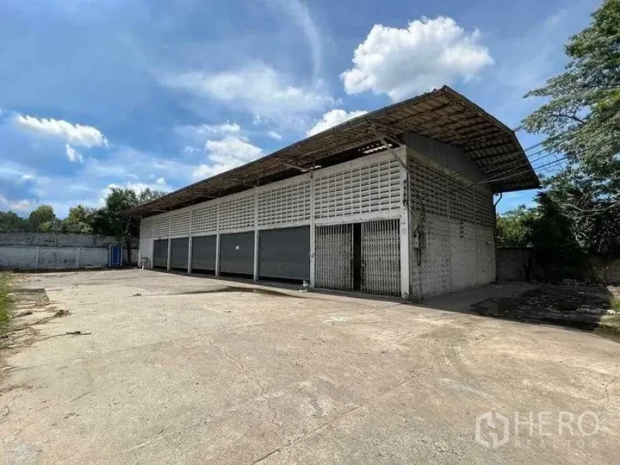 Warehouse for rent in Bang Na, Bangkok - Front exterior of the warehouse showing gated entrance, ventilated block walls, and expansive paved forecourt.