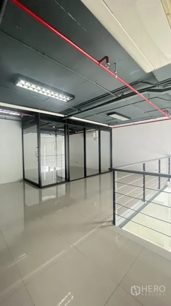 Office Space for rent in Khlong Toei, Bangkok - Mezzanine office area showing exposed ceiling pipes, fluorescent lighting, and glass partitions.