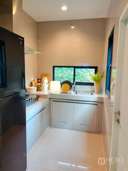 Detached House for rent in Bang Phli, Samut Prakan - Fitted kitchen with countertops, sink by window, cooktop and black fridge.