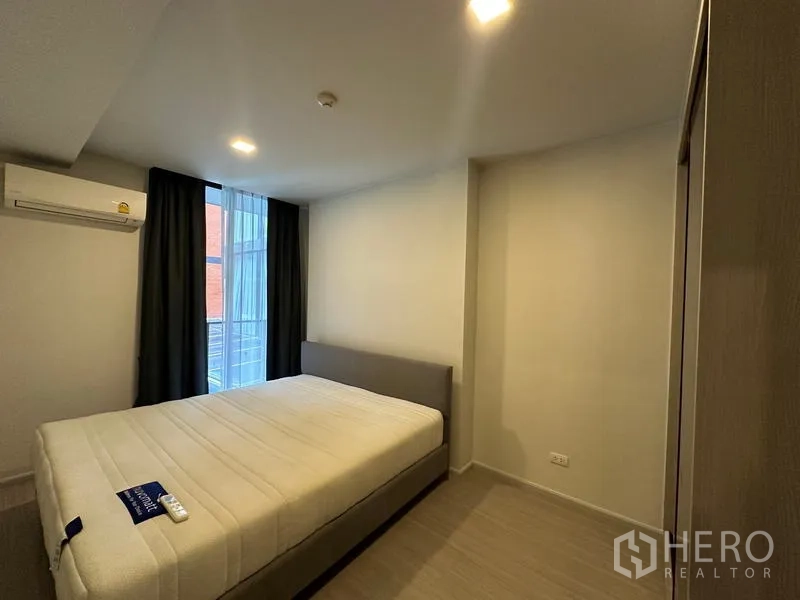 Condominium for rent in Khlong Toei, Bangkok - Cozy bedroom with double bed, wardrobe, air conditioner, and window with blackout curtains.