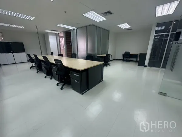 Office Space for rent - Spacious office floor with long wooden desks, storage cabinets, and grid ceiling lighting.