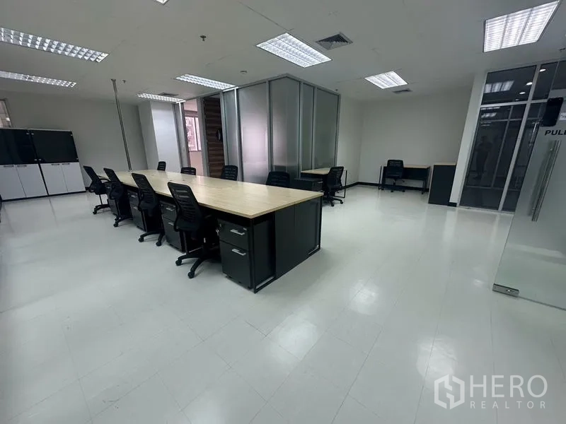 Office Space for rent - Spacious office floor with long wooden desks, storage cabinets, and grid ceiling lighting.