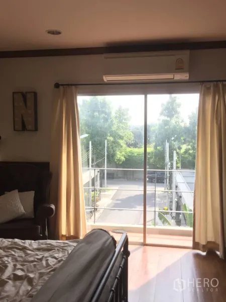 Townhouse for sale in Suan Luang, Bangkok - Bedroom with sliding glass doors to a balcony, air conditioner, and neighborhood view.