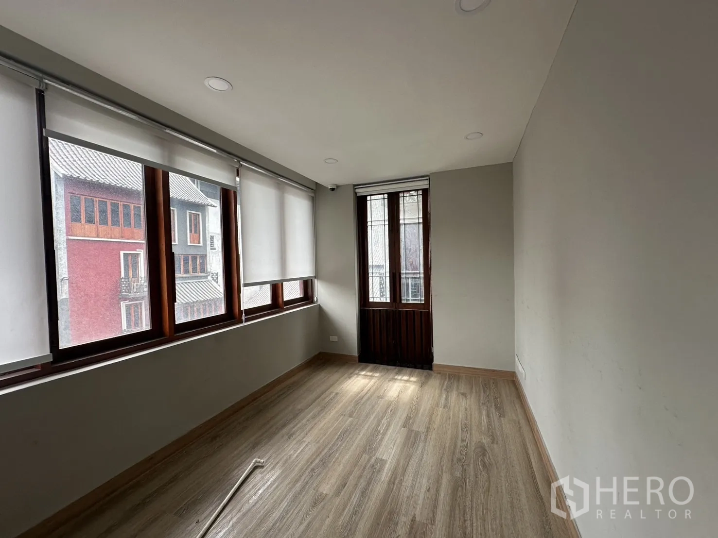 Home Office for rent in Pathum Wan, Bangkok - Compact office room with large windows, roller blinds and a wooden door to balcony.
