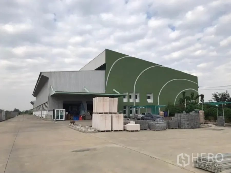 Warehouse for rent in Sai Noi, Nonthaburi - Modern warehouse exterior in Sai Noi with green facade, covered loading bay and wide concrete yard.