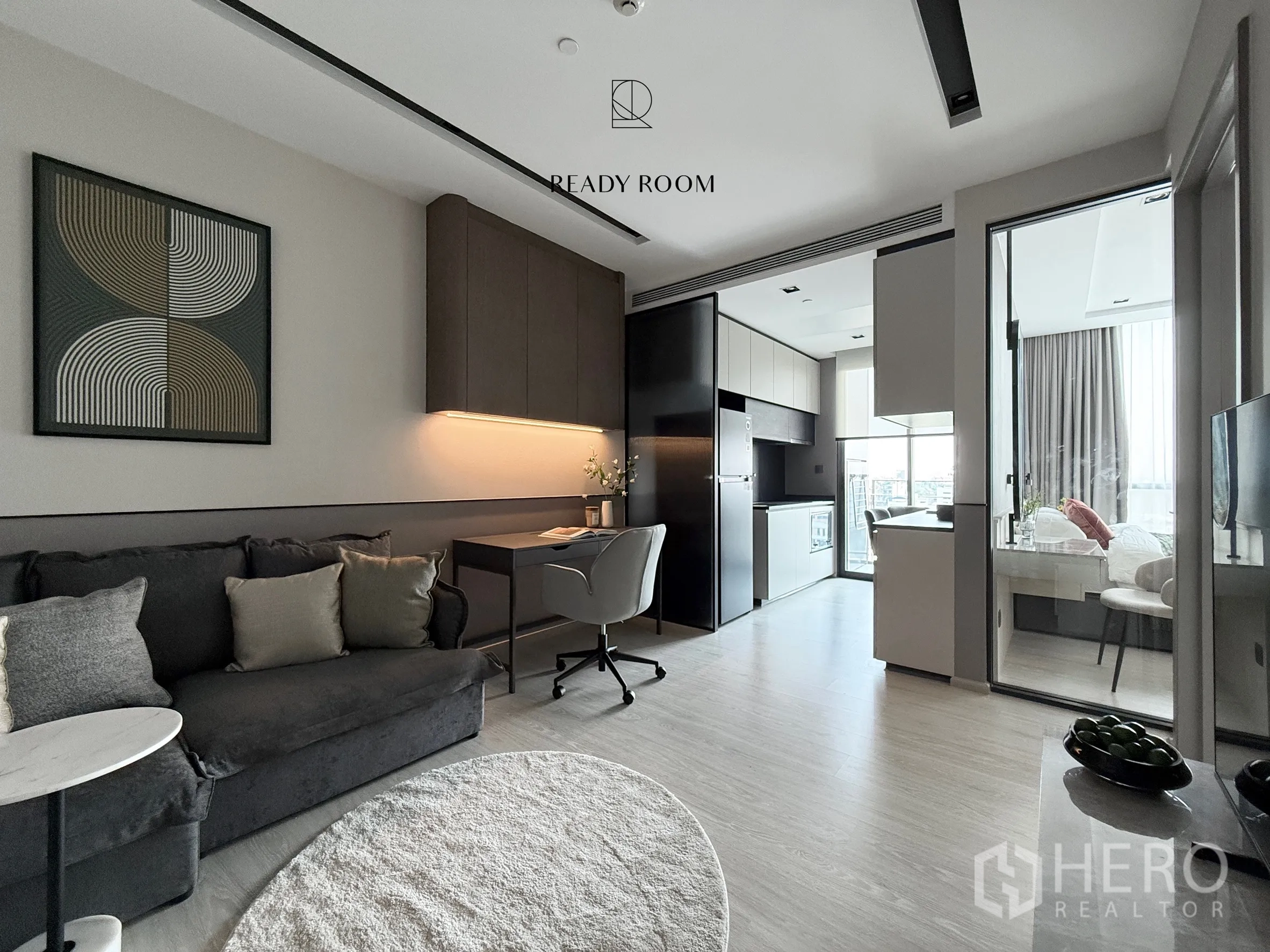 Condominium for rent in Khlong Toei, Bangkok - Open-plan living room with sofa, study desk, kitchen, and glass door to the bedroom.