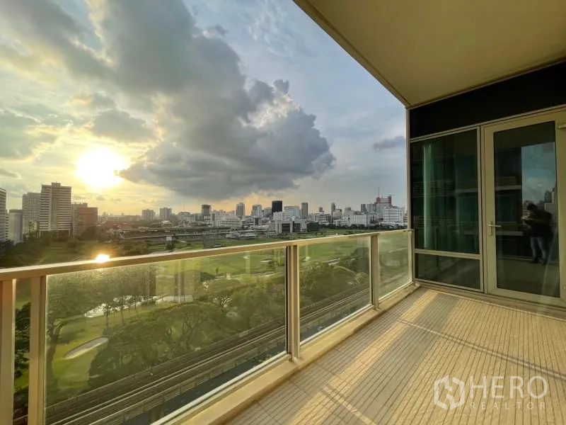 Condominium for rent or sale in Pathum Wan, Bangkok - Spacious balcony at sunset with glass railing overlooking a golf course and city skyline.
