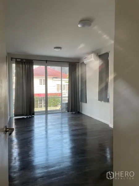 Detached House for rent in Huai Khwang, Bangkok - Sunlit bedroom with dark wood floors, curtains and sliding doors to the balcony.