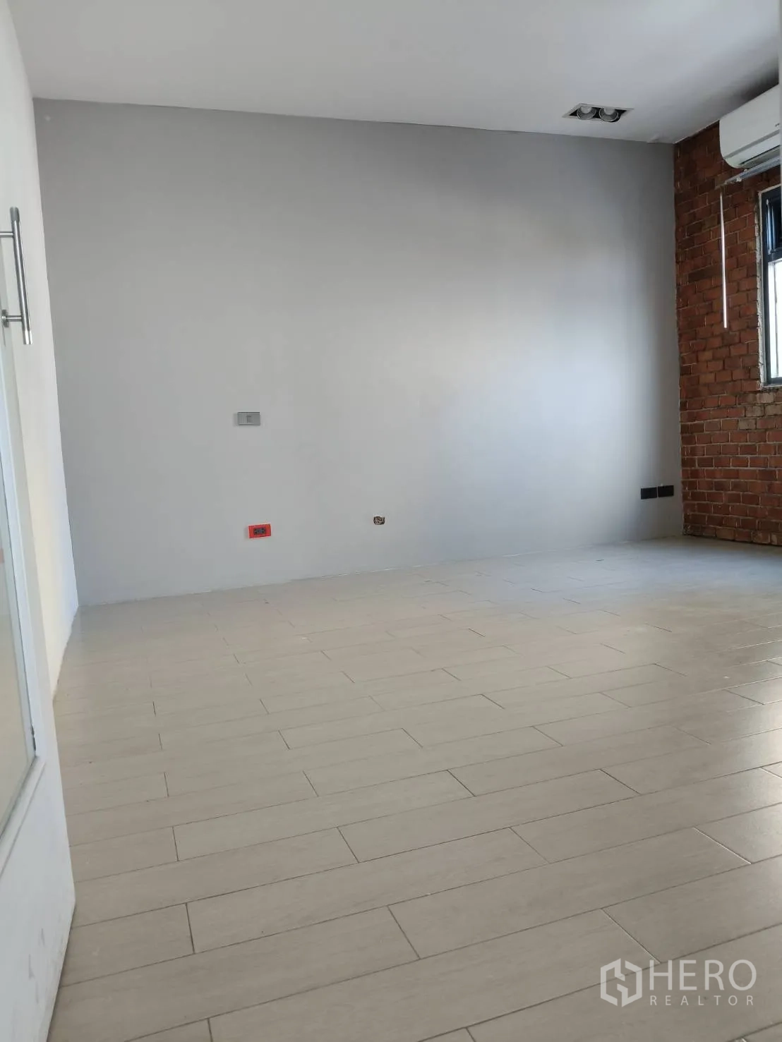 Office Space for rent in Khlong Toei, Bangkok - Spacious room with brick accent wall, air-conditioning and wood-look tile floor.