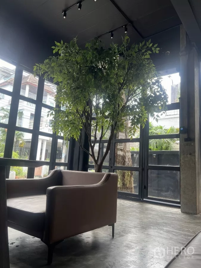 Home Office for rent in Wang Thonglang, Bangkok - Double-height lobby area with a sofa and full-height glass walls around a tree.