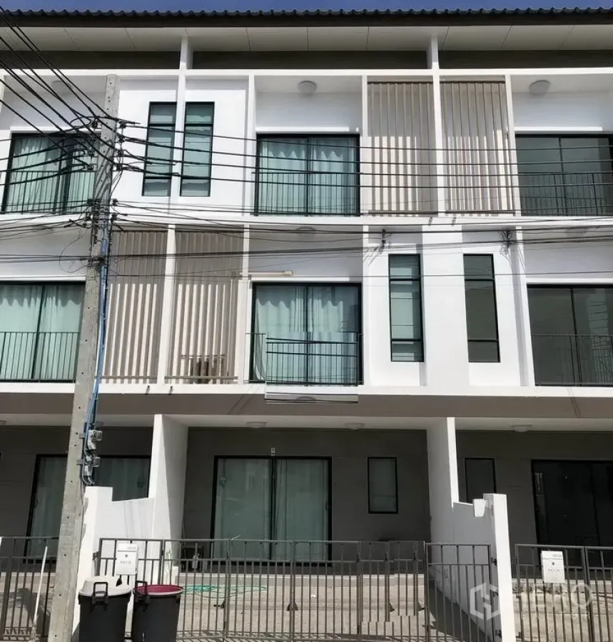 Townhouse for rent in Bang Kapi, Bangkok - Modern three-storey townhouse facade with small balconies, large glass doors and a gated carport.