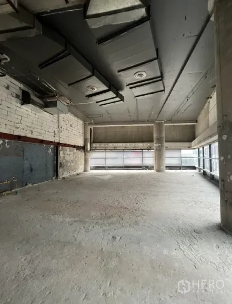 Retail Space for rent - Unfitted open‑plan retail floor with high ceiling, exposed ducting and wide street‑facing windows.