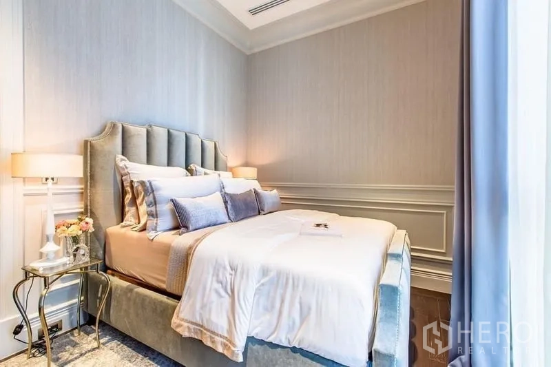 Condominium for sale in Pathum Wan, Bangkok - Cozy bedroom with upholstered bed, wall molding and bedside tables with lamps.