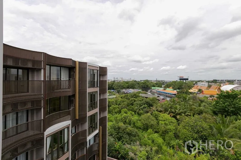 Condominium for sale in Watthana, Bangkok - Modern low‑rise condo facade with curved balconies overlooking lush greenery and skyline in Watthana, Bangkok.