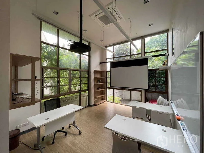 Home Office for rent in Watthana, Bangkok - High-ceiling training room with projector screen and floor-to-ceiling garden windows.