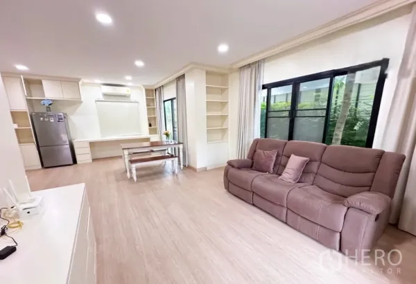 Detached House for sale in Lam Luk Ka, Pathum Thani - Open-plan living area with brown sofa, built-in shelving, dining table and large windows to greenery.