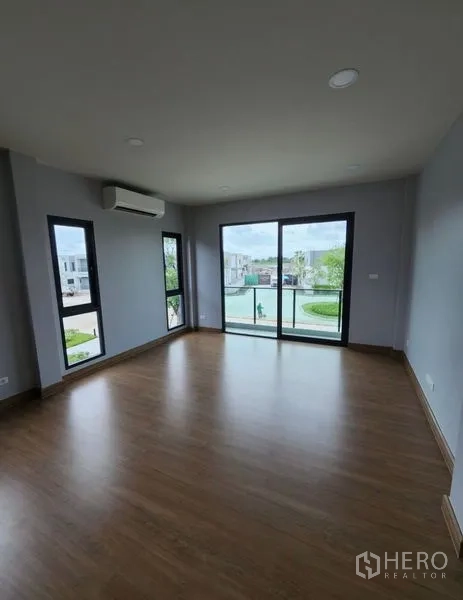 Detached House for rent in Bang Phli, Samut Prakan - Corner living room with wood flooring and large sliding doors opening to balcony and community view.