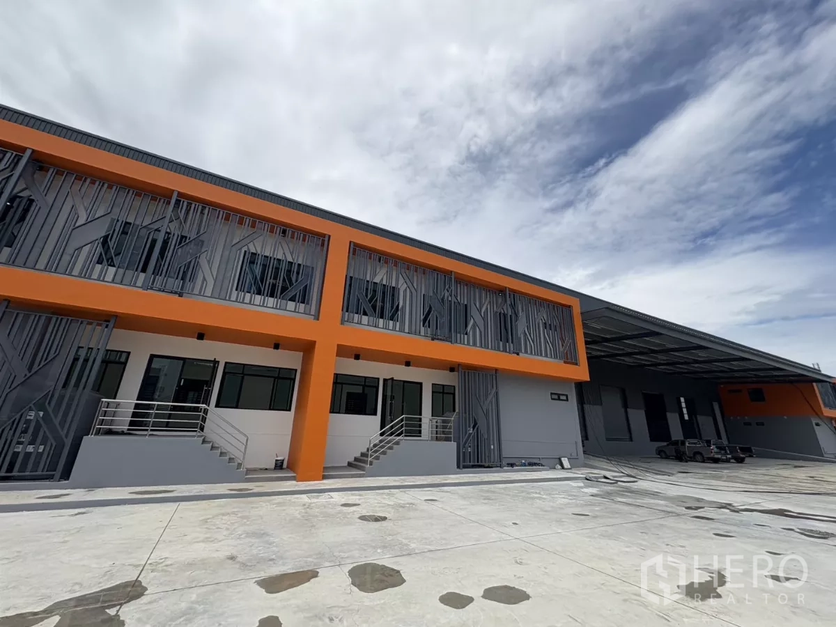 Factory for rent in Bang Pakong, Chachoengsao - Wide view of the modern factory exterior showing a covered loading bay and expansive concrete yard for trucks.