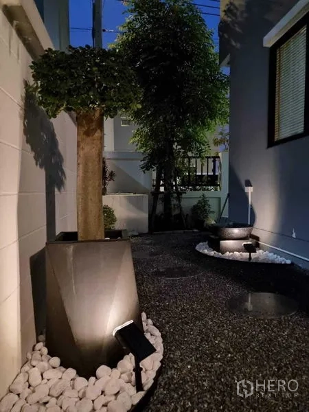 Detached House for sale in Khan Na Yao, Bangkok - Side yard with gravel path, illuminated planters and trees at dusk.