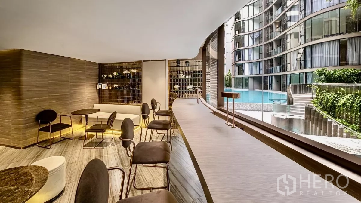 Condominium for rent in Khlong Toei, Bangkok - Residents’ lounge with bar seating and pool view through a glass wall.