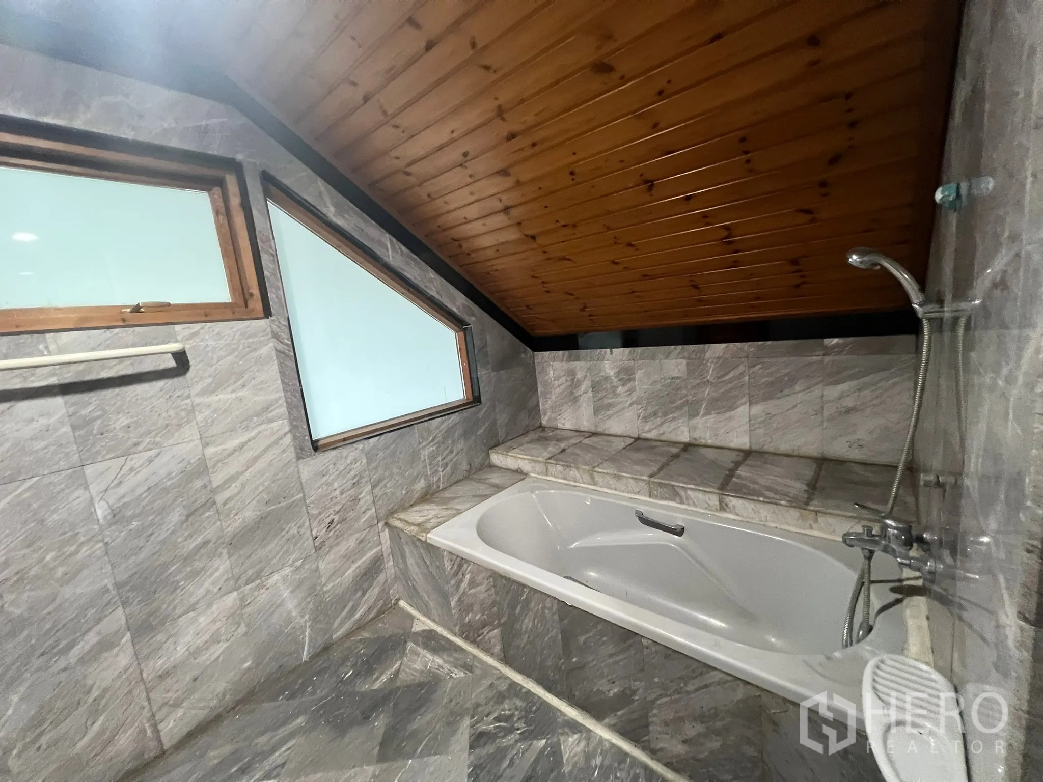 Home Office for rent in Suan Luang, Bangkok - Built-in bathtub beneath a sloped ceiling in a stone-tiled bathroom with frosted windows.