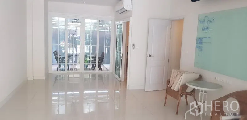Townhouse for rent in Bang Na, Bangkok - Bright living area with glossy tile floors, glass partition to a patio, and wall‑mounted air conditioner.
