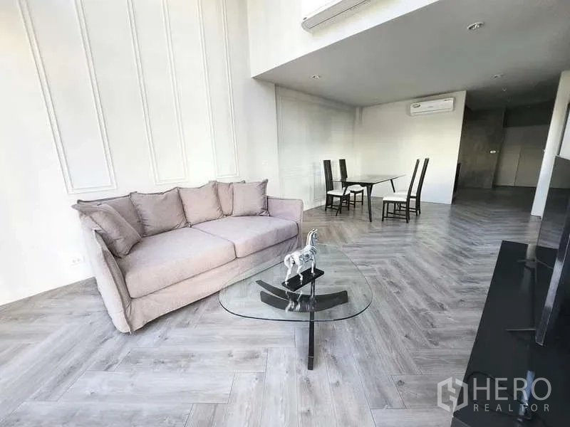 联排别墅 出租在Watthana, Bangkok - 开放式客餐厅，鱼骨拼地板，灰色沙发与玻璃茶几，配空调。