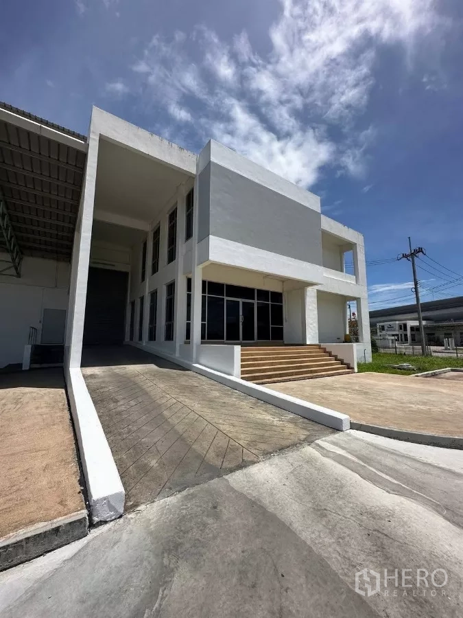 Factory for rent in Si Racha, Chon Buri - Modern two-storey office block with ramp and steps beside the factory under blue sky.