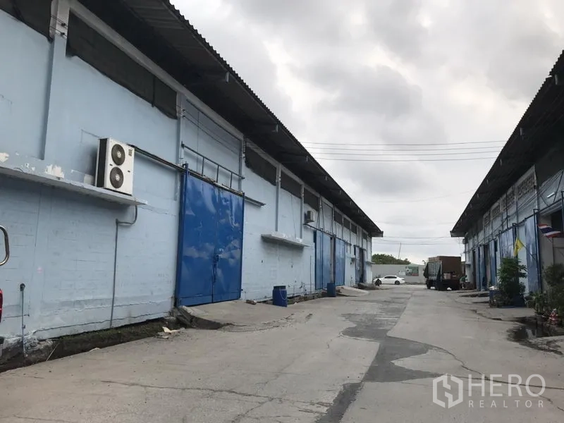 货栈 出租在Bang Phli, Samut Prakan - 两排浅蓝色仓库之间的通道，宽大的蓝色装卸门，卡车出入方便。