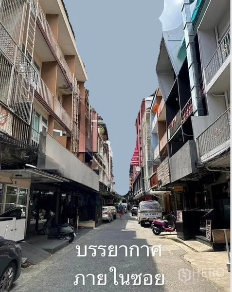 Shophouse for rent or sale in Watthana, Bangkok - Narrow soi lined with multi‑storey shophouses, parked cars and motorbikes in a lively retail lane.