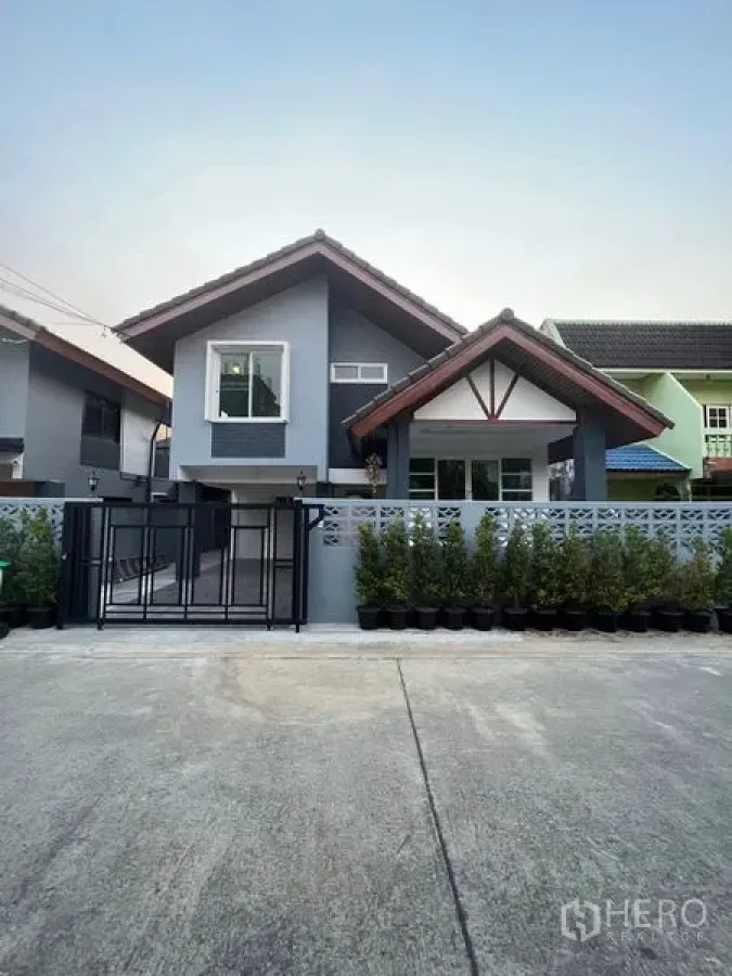 Detached House for rent in Khlong Toei, Bangkok - Front exterior of a grey detached house with gable roof, gated driveway, and potted hedges.