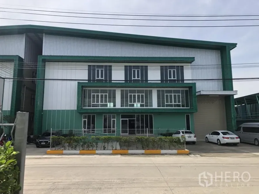 Factory for rent or sale in Bang Phli, Samut Prakan - Modern green-and-white factory facade with gated parking and a large roller shutter.