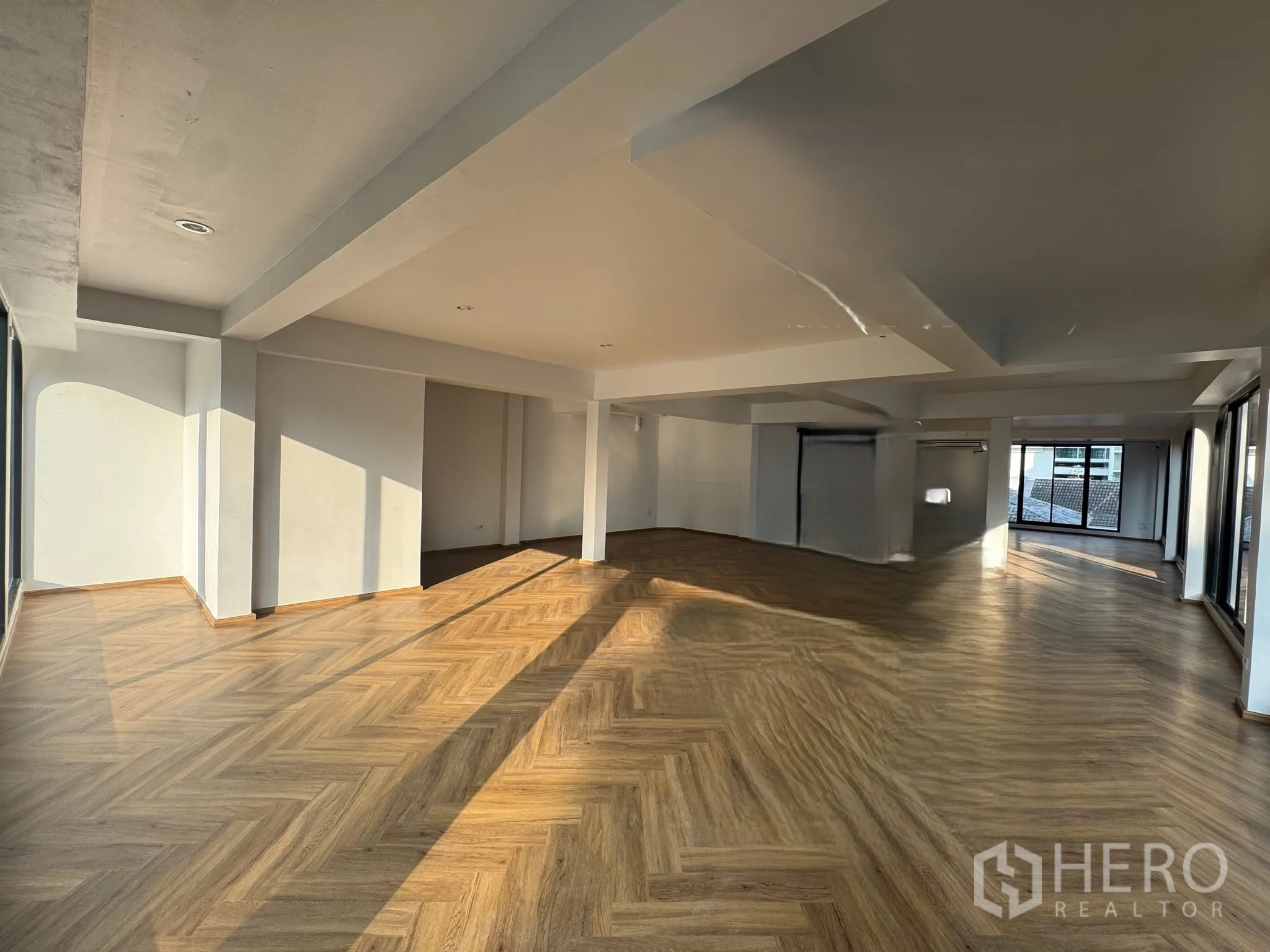 พื้นที่ขายของ for rent in Watthana, Bangkok - พื้นที่ค้าปลีกแบบโอเพ่น โปร่งสว่าง พื้นไม้ลายก้างปลา ผนังสีขาว และหน้าต่างกระจกบานใหญ่รับแสงธรรมชาติ