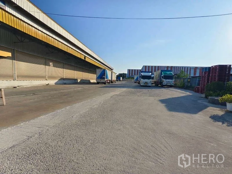 货栈 出租在Samut Prakan - 仓库旁宽阔混凝土场地，卡车停靠便于装卸与调头。