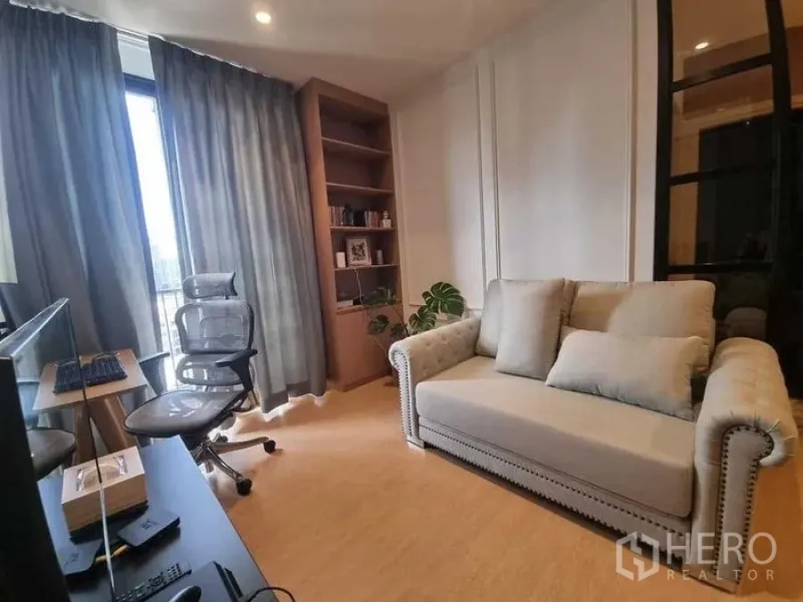 Condominium for rent in Watthana, Bangkok - Bright living room and study area with sofa, desk, gray curtains, built-in shelving, and balcony access.