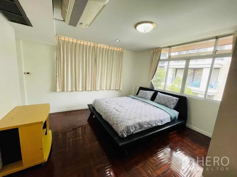 Detached House for rent in Watthana, Bangkok - Guest bedroom with large windows, curtains, and dark wood flooring.