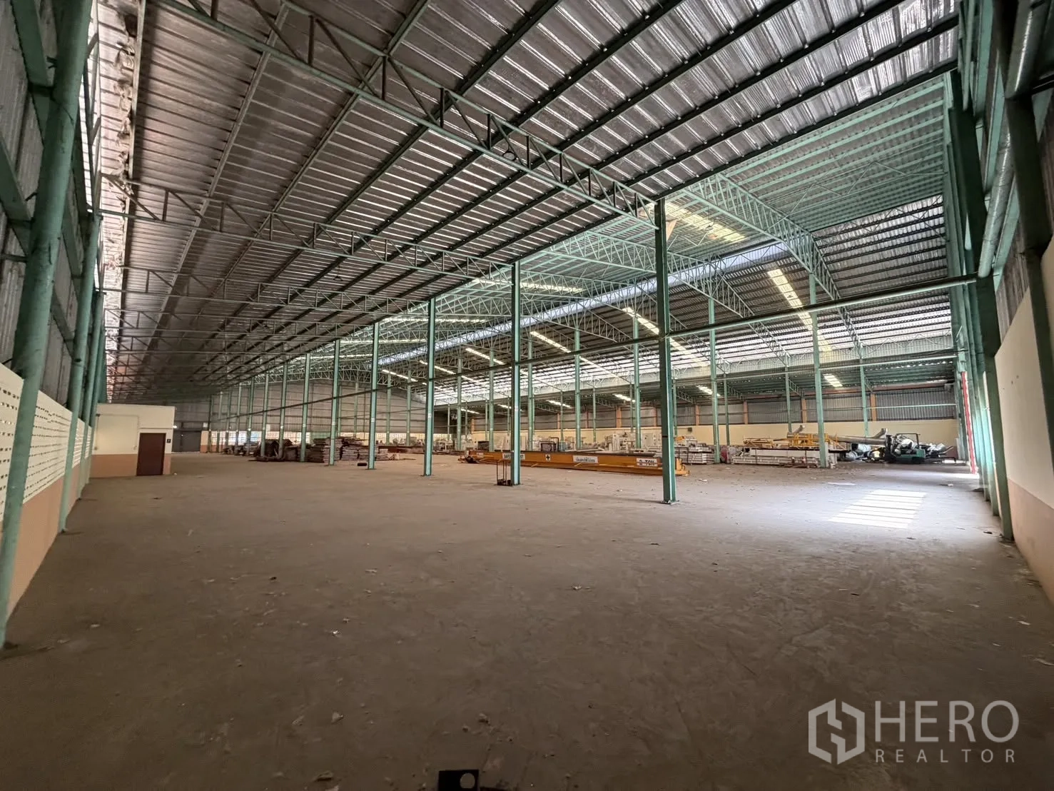 Factory for rent in Bang Na, Bangkok - Vast factory interior with high metal roof, green steel columns, and a concrete floor.