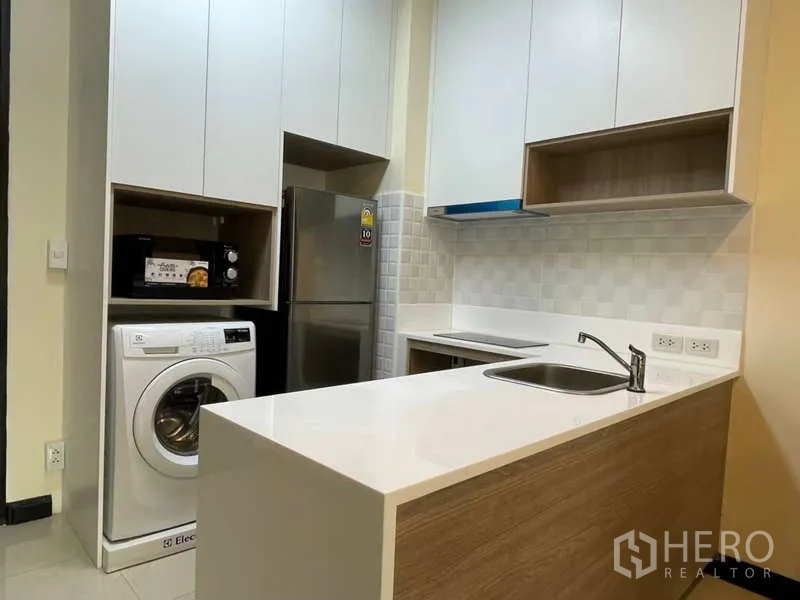 Apartment for rent in Khlong Toei, Bangkok - Modern kitchen with white cabinets, refrigerator, microwave and washing machine.