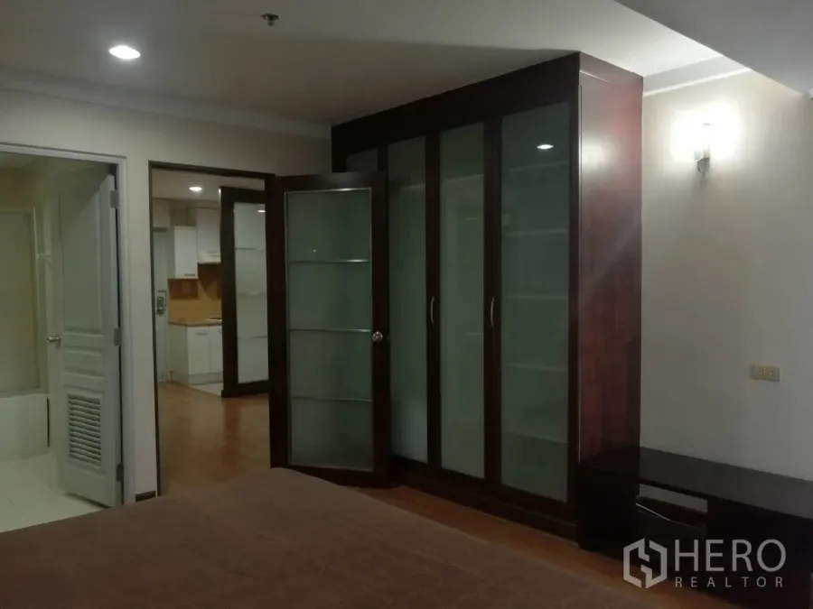 Condominium for rent in Khlong Toei, Bangkok - Bedroom with large glass-front wardrobe, view to kitchen and bathroom.
