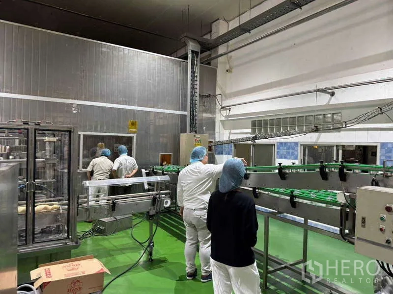 Factory for sale in Samut Prakan - Stainless conveyor system beside insulated walls and control panels in the factory.