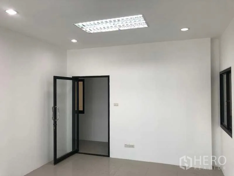 Factory for rent or sale in Samut Prakan - Bright office room with glass door, recessed lights and tiled flooring.