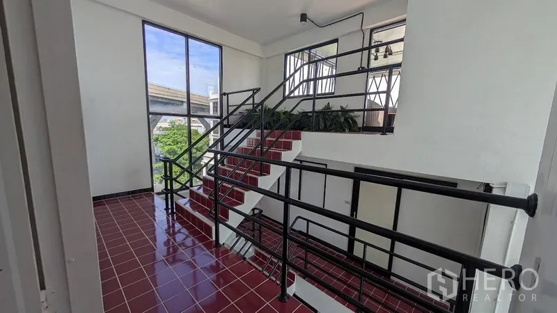 Home Office for rent or sale in Phra Khanong, Bangkok - Stair landing with glossy red tiles, large windows and black handrails.