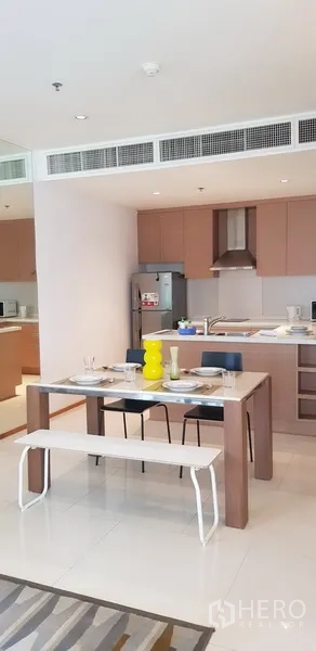 Condominium for rent in Khlong Toei, Bangkok - Open dining space beside modern kitchen with cabinets and stainless fridge.